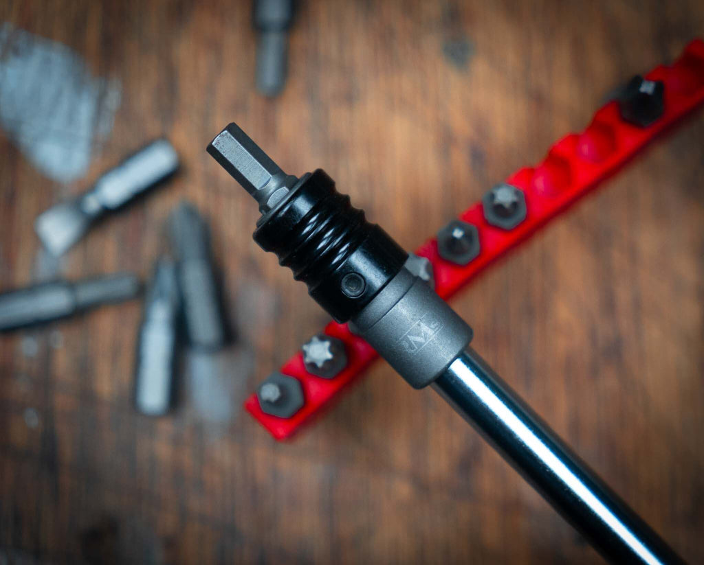 1/4" adaptor with quick-release bit chuck for motorcycle toolkits, surrounded by additional bits on a wooden surface.